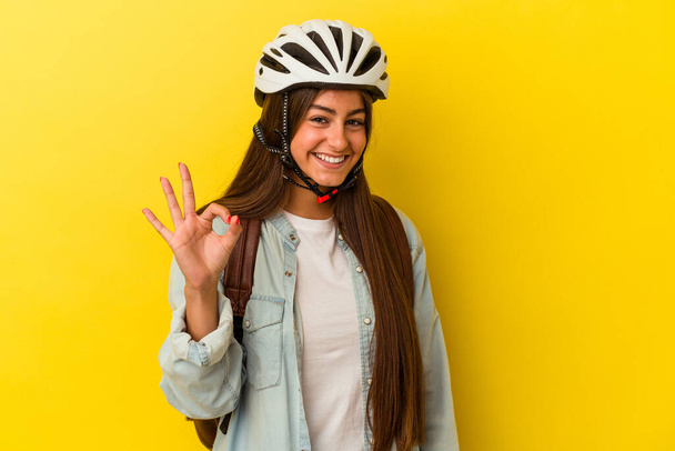 młody student biały kobieta noszenie a rower kask izolowane na żółty tło wesoły i pewny pokazując ok gest. - Zdjęcie, obraz