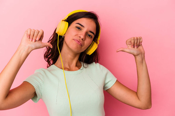 Jovem caucasiana ouvindo música isolada em fundo rosa se sente orgulhoso e auto-confiante, exemplo a seguir. - Foto, Imagem