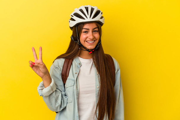 Nuori opiskelija valkoihoinen nainen yllään pyöräilykypärä eristetty keltaisella taustalla osoittaa numero kaksi sormilla. - Valokuva, kuva