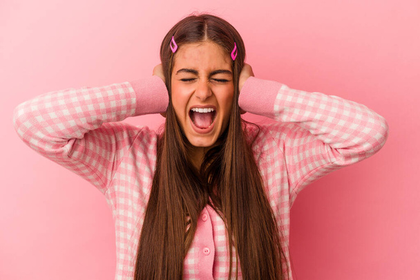 Junge kaukasische Frau isoliert auf rosa Hintergrund bedeckt Ohren mit Händen versuchen, nicht zu laute Geräusche zu hören. - Foto, Bild