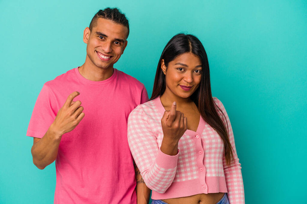 Joven pareja latina aislada sobre fondo azul señalándote con el dedo como si invitaras a acercarte. - Foto, Imagen