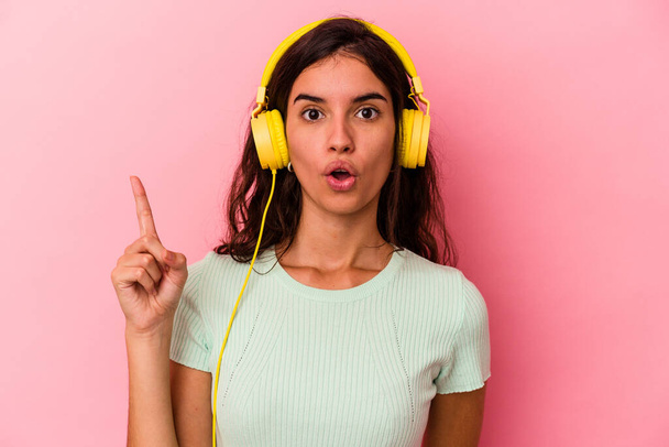 Young caucasian woman listening music isolated on pink background having some great idea, concept of creativity. - Photo, Image