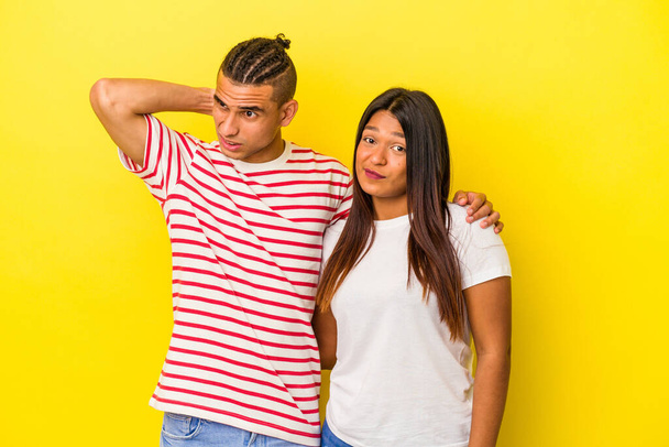 Joven pareja latina aislada sobre fondo amarillo tocando la parte posterior de la cabeza, pensando y haciendo una elección. - Foto, Imagen