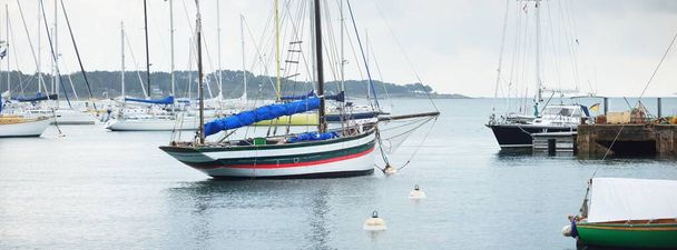 An elegant old gaff rigged classic boat anchored on mooring near the ocean shore, close-up. Brittany, France. Transportation, sailing, racing, regatta, sport and leisure activity, vacations, cruise - Photo, Image