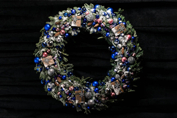 christmas wreath on a dark background. Christmas wreath with red and silver bauble decorations, bow, holly, mistletoe, pine cones and blue spruce fir - Foto, afbeelding