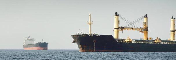 Grand navire-grue à cargaison noire ancré dans le détroit de Gibraltar. Une vue depuis le yacht. Summer Atlantic navigue près de l'Espagne et de l'Afrique. Transport de marchandises, logistique, industrie, thème des communications mondiales - Photo, image