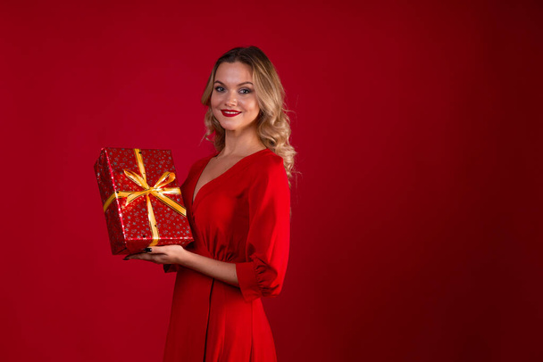 Give gifts for the holiday. Cheerful young woman in a red dress with a red gift box in her hands. - Foto, Imagen