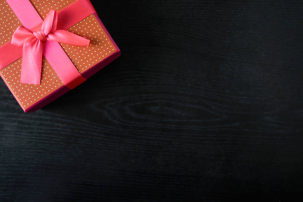 Rode geschenkdoos met roze strikje op de achtergrond van zwart hout. Plaats voor tekst - Foto, afbeelding