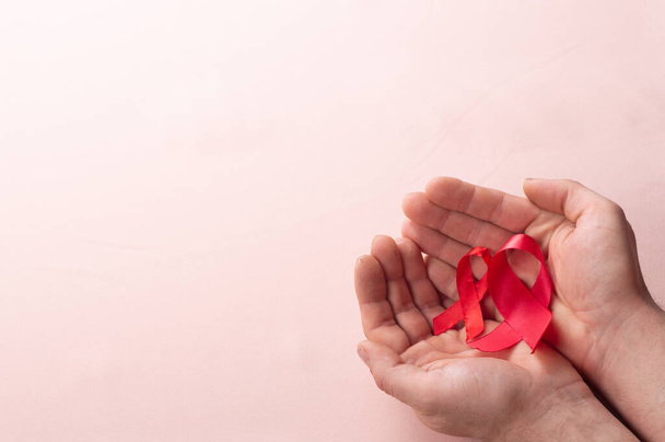 healthcare and medicine concept two hands holding red ribbons HIV and AIDS awareness on brown background close up - Fotó, kép