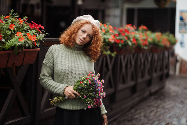 Bere kazaklı bir kadın portresi. Elinde restoranın arka planında bir buket çiçek var.  - Fotoğraf, Görsel