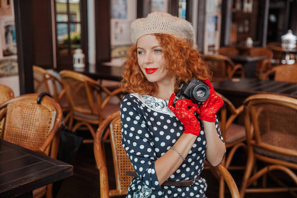 Eine Frau mit Baskenmütze und Vintage-Kleid hält eine Kamera in der Hand und schießt - Foto, Bild