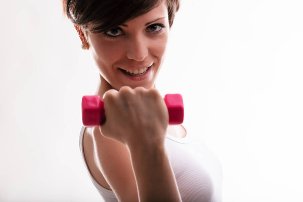 Determined young woman working out with weights lifting a dumbbell in her hand in close up with focus to her face - Photo, Image