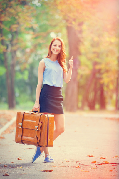 ευτυχής κοκκινομάλλα κορίτσι με τη βαλίτσα στο πάρκο φθινόπωρο. - Φωτογραφία, εικόνα