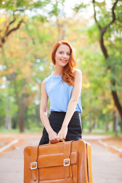 glückliches rothaariges Mädchen mit Koffer im Herbstpark. - Foto, Bild