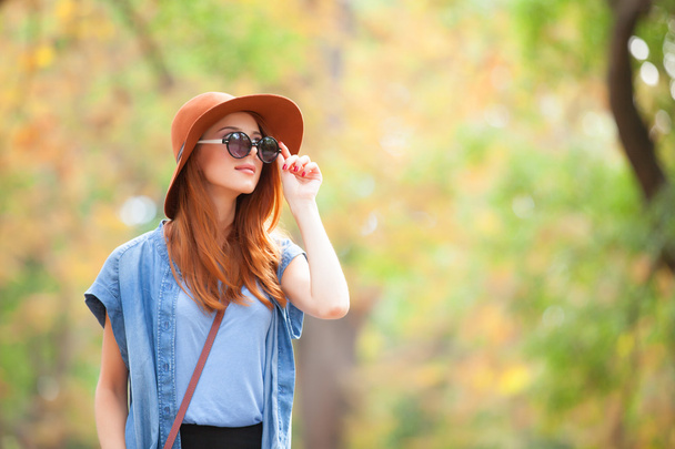 Redhead girl in sunglasses and hat in the autumn park. - Valokuva, kuva