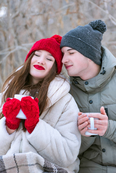 Jovem casal amoroso no inverno ao ar livre. Menina em chapéu vermelho e mitenes segura caneca - Foto, Imagem