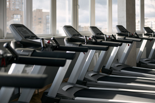 Side view of empty treadmills on wooden floor near panoramic window in fitness club. Side view. - Photo, Image