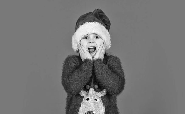 Adorable girl wear santa claus hat red background. Emotional face expression. Happy childhood. Counting days till christmas. Christmas party. Can not hold back emotions. Christmas holiday invitation - Foto, Bild