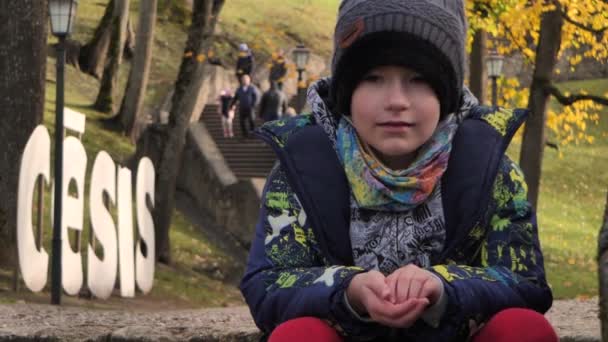 Chłopiec siedzi na dużych schodach w parku jesienią - Materiał filmowy, wideo