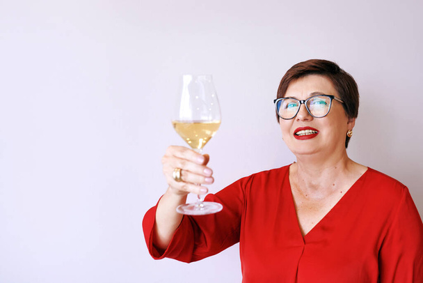 стильная зрелая пожилая женщина в красной блузке с бокалом белого вина, празднующего Новый год. Веселье, вечеринка, стиль жизни, алкоголь, концепция праздника - Фото, изображение