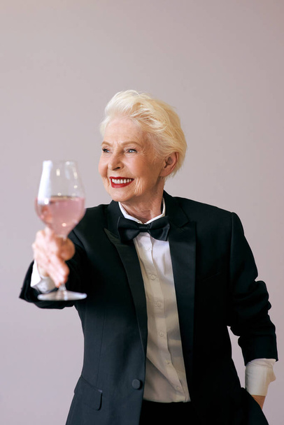 стильный зрелый сомелье пожилая женщина в смокинге с бокалом вина. Веселье, вечеринка, стиль жизни, работа, алкоголь, концепция празднования - Фото, изображение