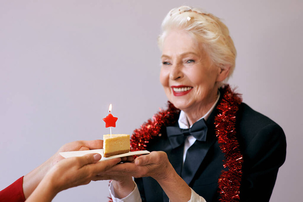 anziana donna elegante in smoking soffiando candela sulla sua torta di compleanno. Stile di vita, positivo, moda, concetto di stile - Foto, immagini