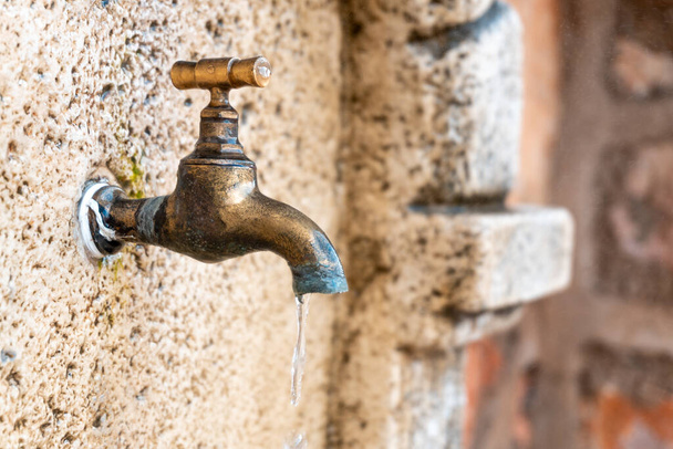Close-up with selective focus to a metal faucet dripping into a fountain. - 写真・画像
