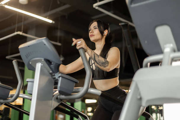 Joven mujer de fitness haciendo ejercicio de cardo en la máquina de ejercicios en el gimnasio. Estilo de vida saludable, concepto deportivo - Foto, Imagen