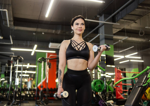 Jeune femme de fitness travaillant biceps avec haltères dans la salle de gym - Photo, image