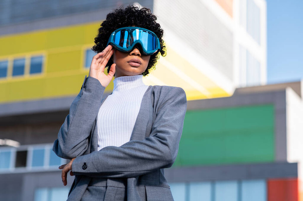A cool young African American lady with curly hair wearing ski goggles in a residential area - Fotoğraf, Görsel