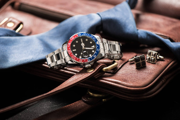 Herrenzubehör, Nahaufnahme an der Armbanduhr mit schwarzem Zifferblatt blau-rote Lünette und Edelstahlarmband. - Foto, Bild