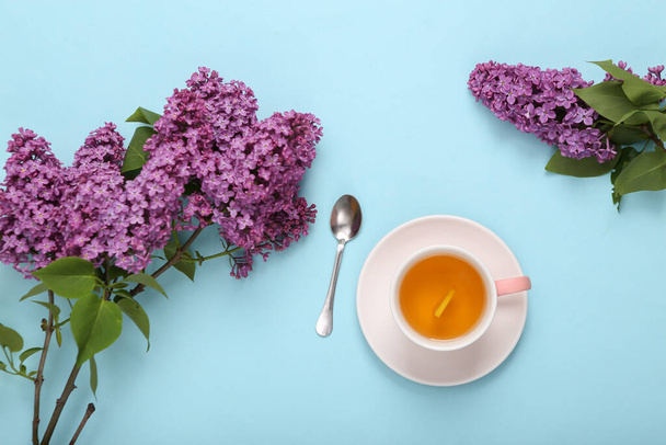 Kuppi mustaa aromaattista teetä sitruunalla ja kukkivien syreenien oksat sinisellä pastellitaustalla. Huippunäkymä. Litteä - Valokuva, kuva