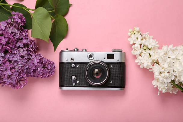Retro camera with branches of blooming lilacs on pink background. Spring concept. Top view. Flat lay - Photo, Image