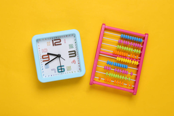 Alarm clock and toy abacus on yellow background - Photo, Image