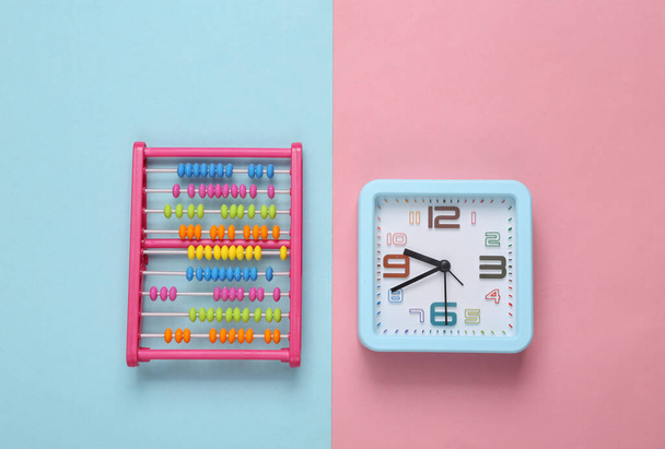 Wekker klok en speelgoed abacus op roze blauwe achtergrond - Foto, afbeelding