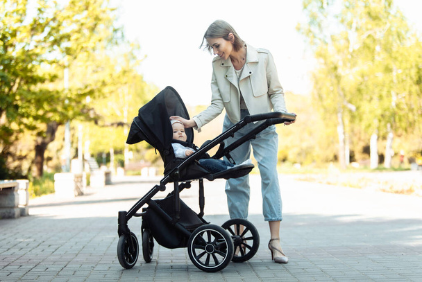 Portret troskliwej matki z córeczką w wózku w parku - Zdjęcie, obraz