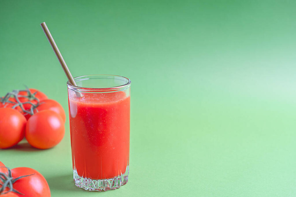 Portion of organic tomato juice made of blended ripe red tomatoes served in tall drinking glass with paper straw against bright green background with ingredients. Image with copy space, horizontal - Fotoğraf, Görsel