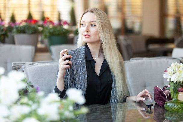 Mladý atraktivní kráska žena blondýny sypání s parfémem na letní terase kavárny - Fotografie, Obrázek
