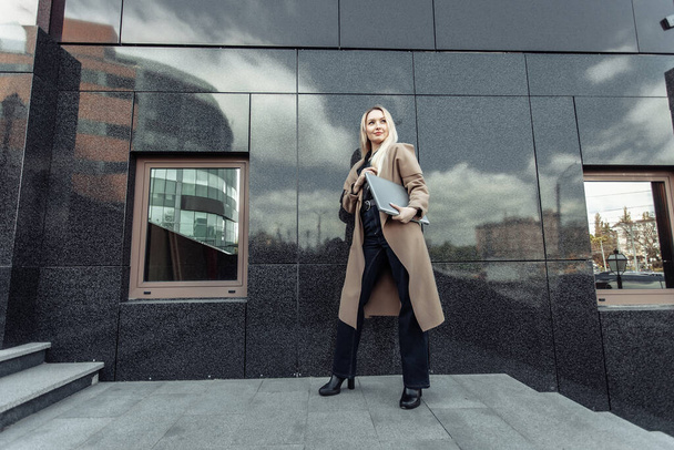 Stylish blonde business woman with laptop in trench coat in urban location - Photo, image