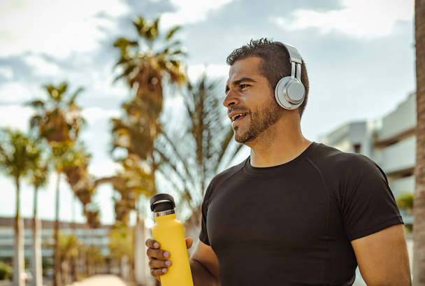 Homme hispanique faisant du jogging et de la routine d'entraînement tout en écoutant de la musique avec écouteurs sans fil en plein air - Photo, image