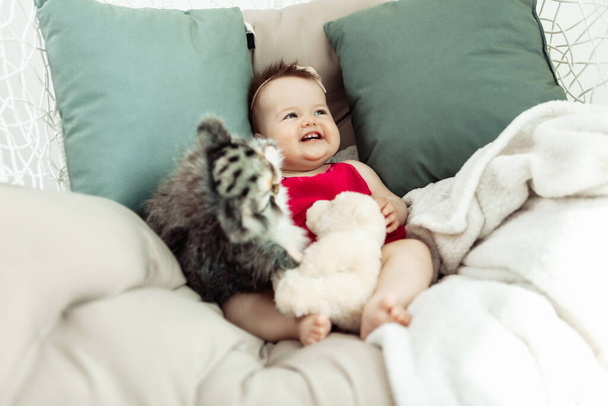 Милая улыбающаяся маленькая девочка лежит на кровати с плюшевыми игрушками. Детство - Фото, изображение