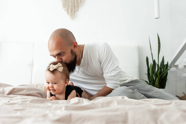Padre cariñoso besa a su hermosa hija en la cabeza en la cama en el dormitorio. Amor y cuidado, concepto familiar feliz - Foto, imagen