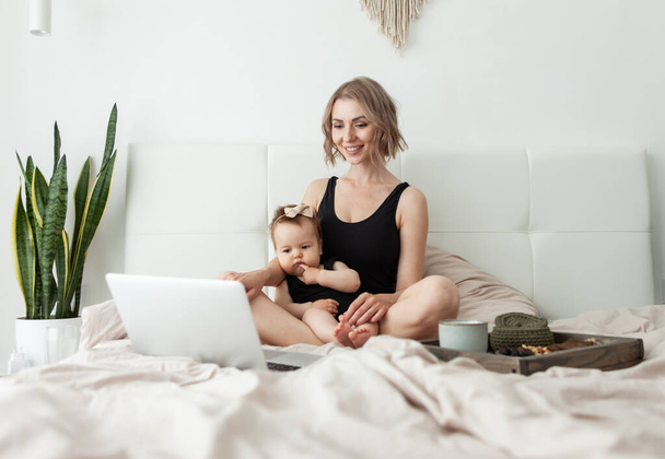 Nette Mutter mit ihrer kleinen Tochter schaut ein Video oder Film im Laptop und frühstückt im Bett. Glückliche Familie. Verbringen Sie Zeit miteinander. Liebe und Fürsorge - Foto, Bild