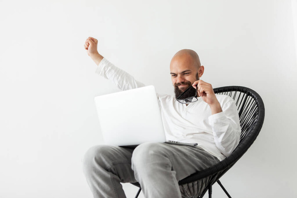 Excited lucky young bearded freelancer sitting in chair with laptop, raised fists up celebrating success, making yes gesture, got promoted, won lottery, victory concept - Photo, Image