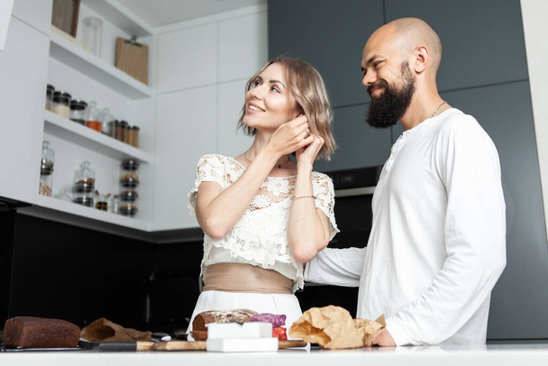 Młoda atrakcyjna kobieta przymierza kolczyki prezentowane przez kochającego męża w kuchni. Romantyczna, miłosna koncepcja - Zdjęcie, obraz