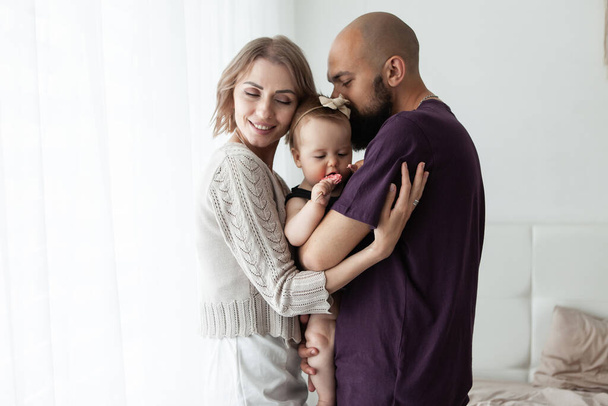 Mom and Dad hug their cute little daughter in the room. Happy family concept - Photo, Image