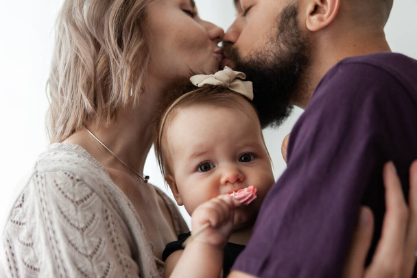 Mamá y papá abrazan a su linda hijita y se besan. Concepto de familia feliz - Foto, Imagen
