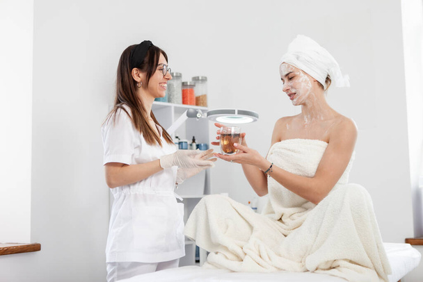 Woman beautician treats her client with cup of tea. Beauty woman in beauty salon. Facial skin care - Photo, Image