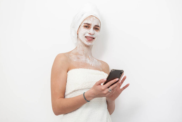 Beautiful woman with facial mask uses smartphone on white background. Skin care concept - Foto, immagini