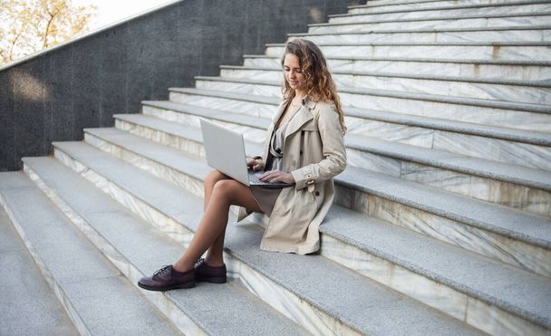 Jonge vrouw student met behulp van laptop terwijl zitten op de trap buiten - Foto, afbeelding